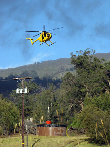 A Windward Aviation helicopter dips water from a ranch tank.